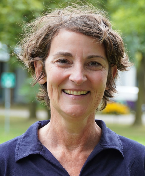 Portrait of a white woman smiling at the camera, in front of a blurred background of greenery