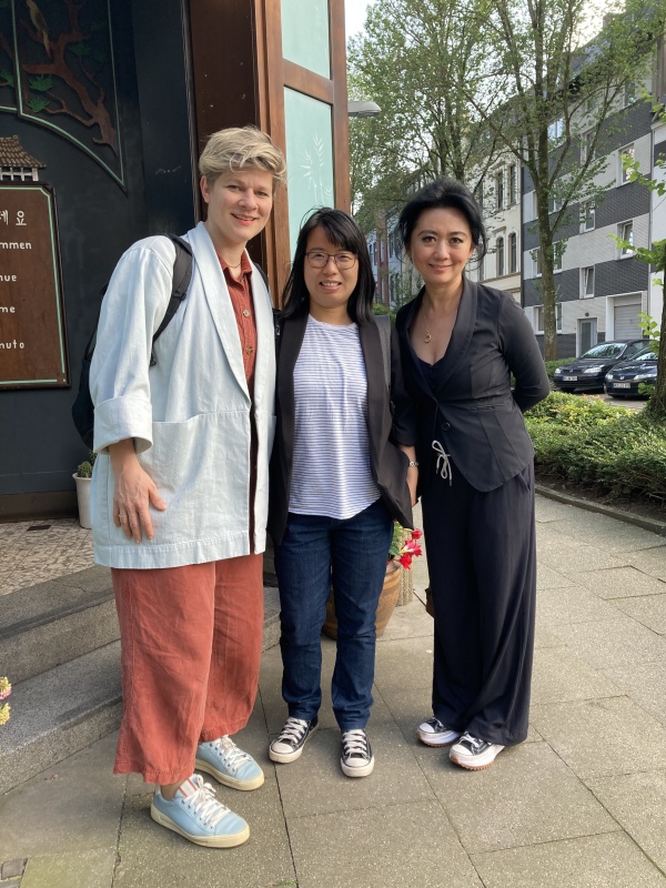 Photo of Jessica Schwittek, Xiaorong Gu, and Jiayiin Li-Gottwald, smiling at the camera and standing on a sidewalk in a residential area