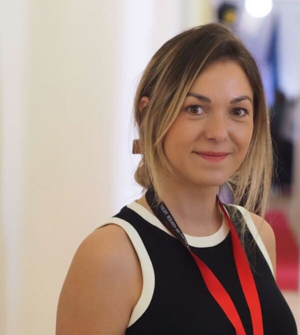 Portrait of a white woman smiling at a camera with a red landyard and ID badge around her neck.