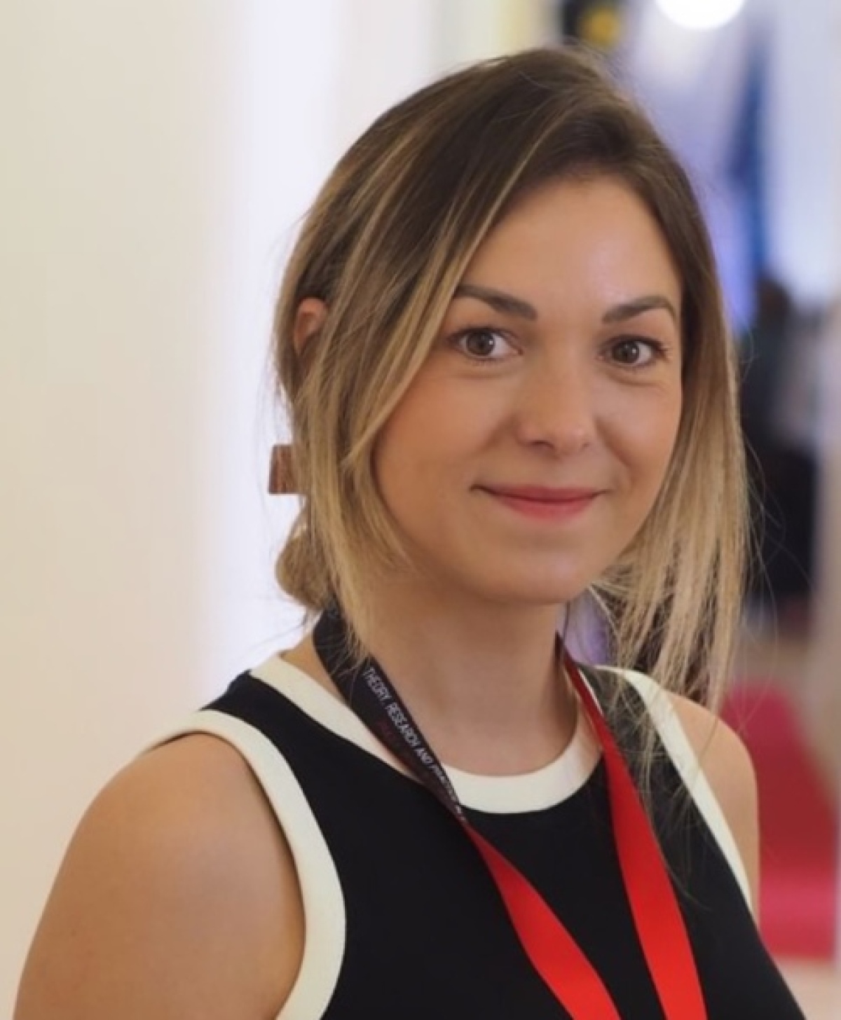 Portrait of Katarzyna Jendrzey, a white woman, smiling at a camera with a red landyard and ID badge around her neck.