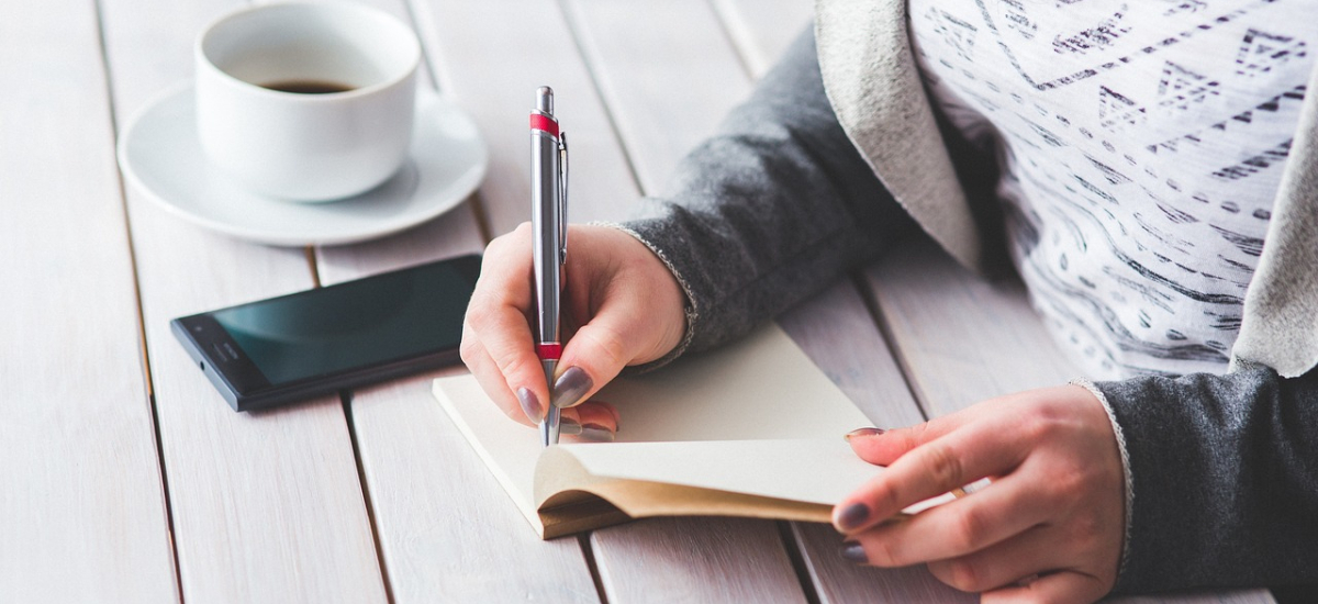 Frau schriebt ins Notizbuch mit Kaffee